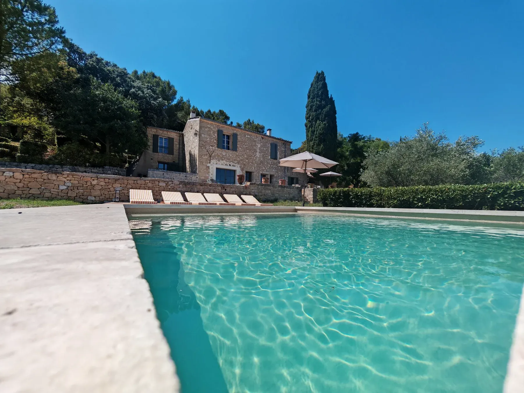 A stone villa and shaded loungers beyond a clear outdoor swimming pool.