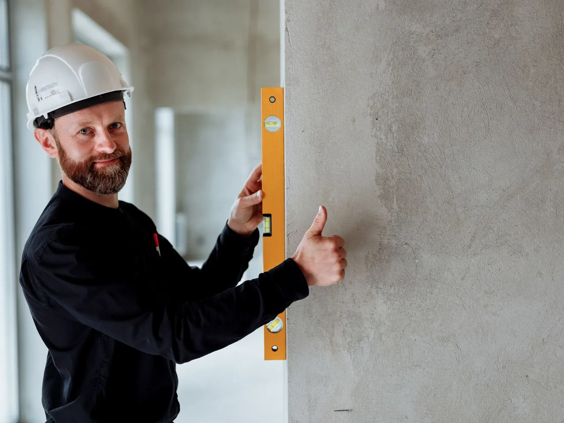 A building specialist in a hard hat checking a plastered wall with a spirit level.